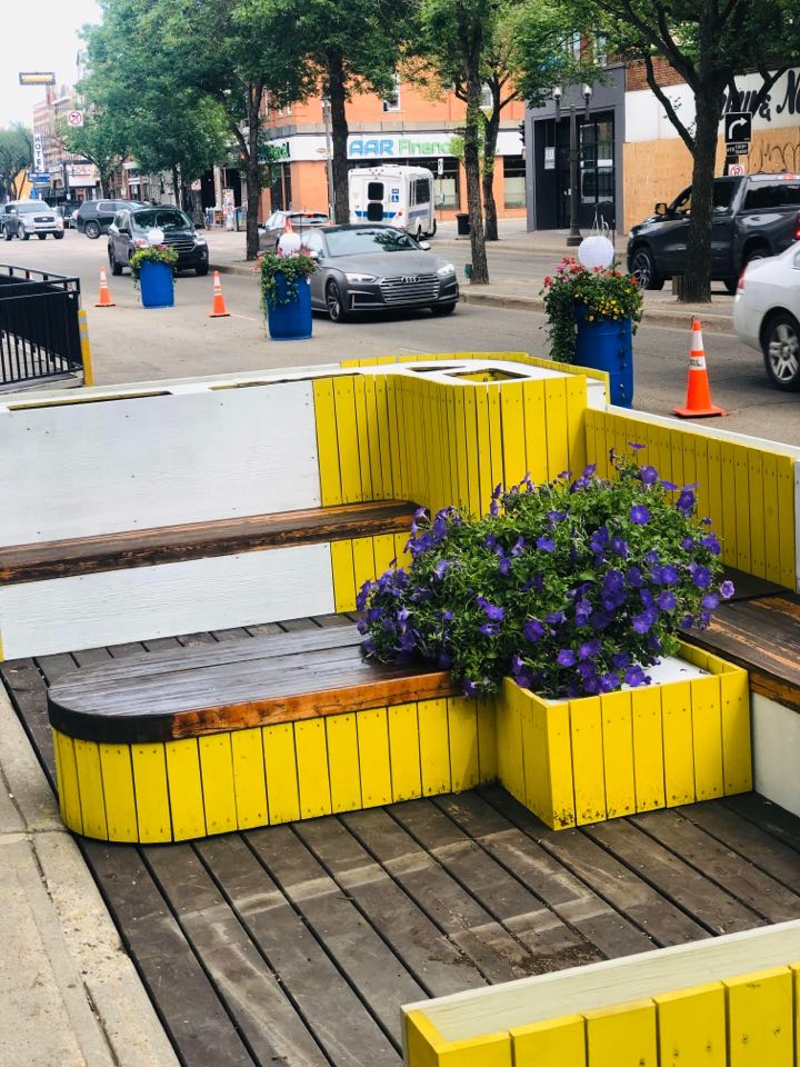 A wooden parklet painted yellow with flowers planted in the middle