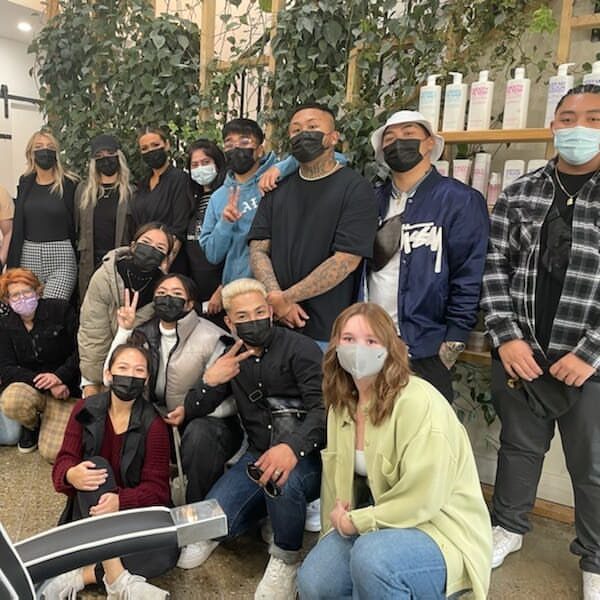 Masked students pose in front of a living plant wall