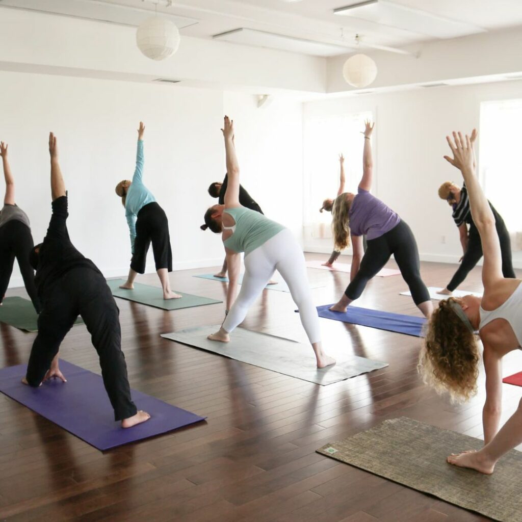 A group of yoga participants reach upwards with their right arms while leaning left