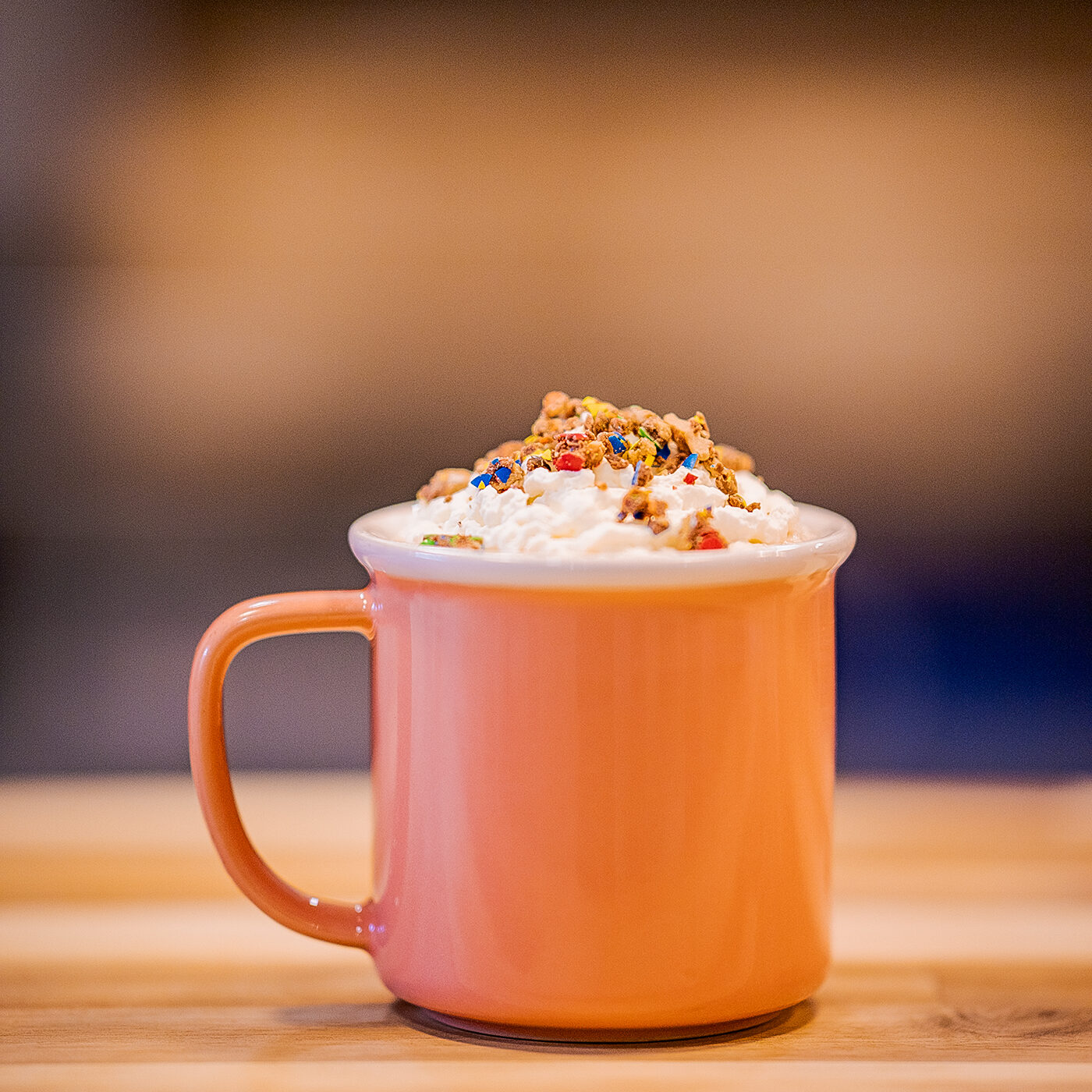 A small orange mug is topped with whipped cream and colourful crumbles of Reese's Pieces