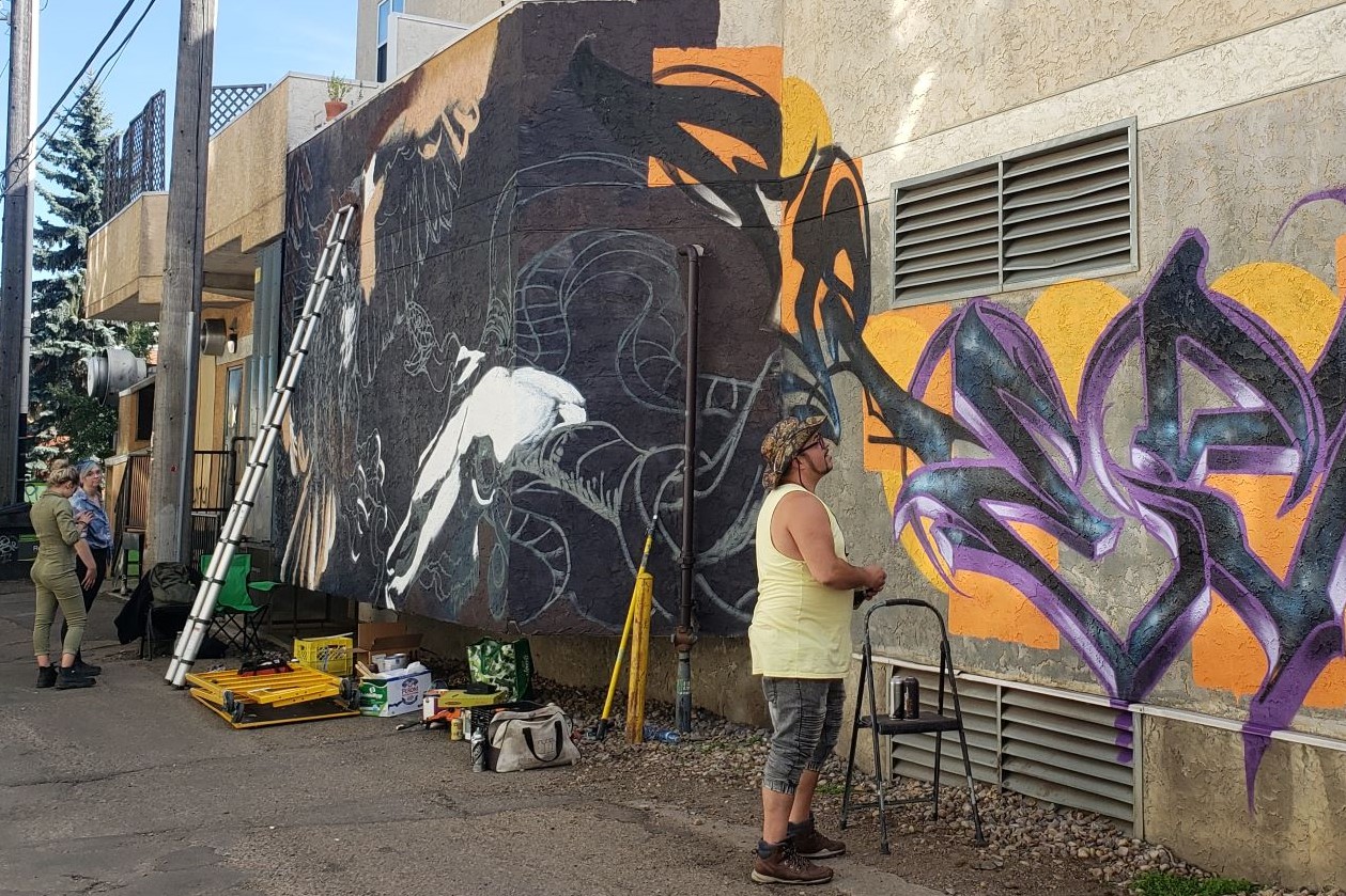 Artists stand back and look at their mural works in progress on a wall